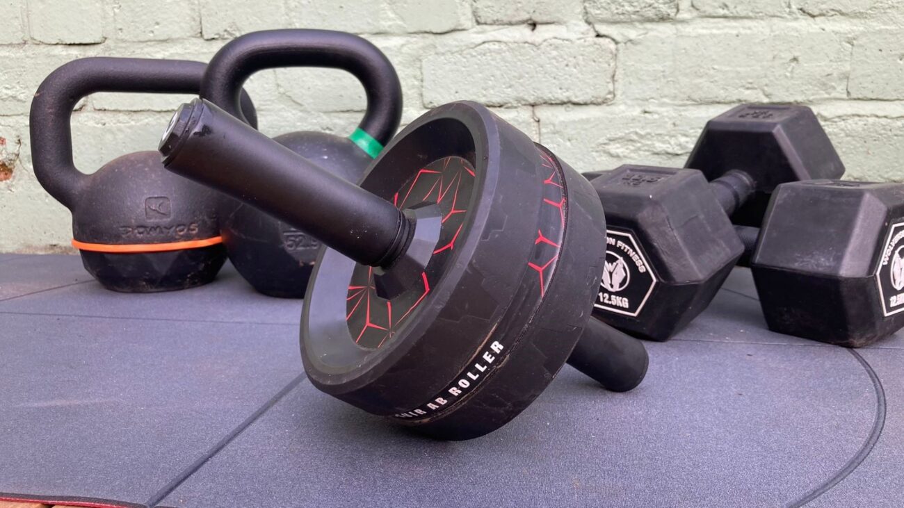 Ab roller on an exercise mat with dumbbells and kettlebells behind it