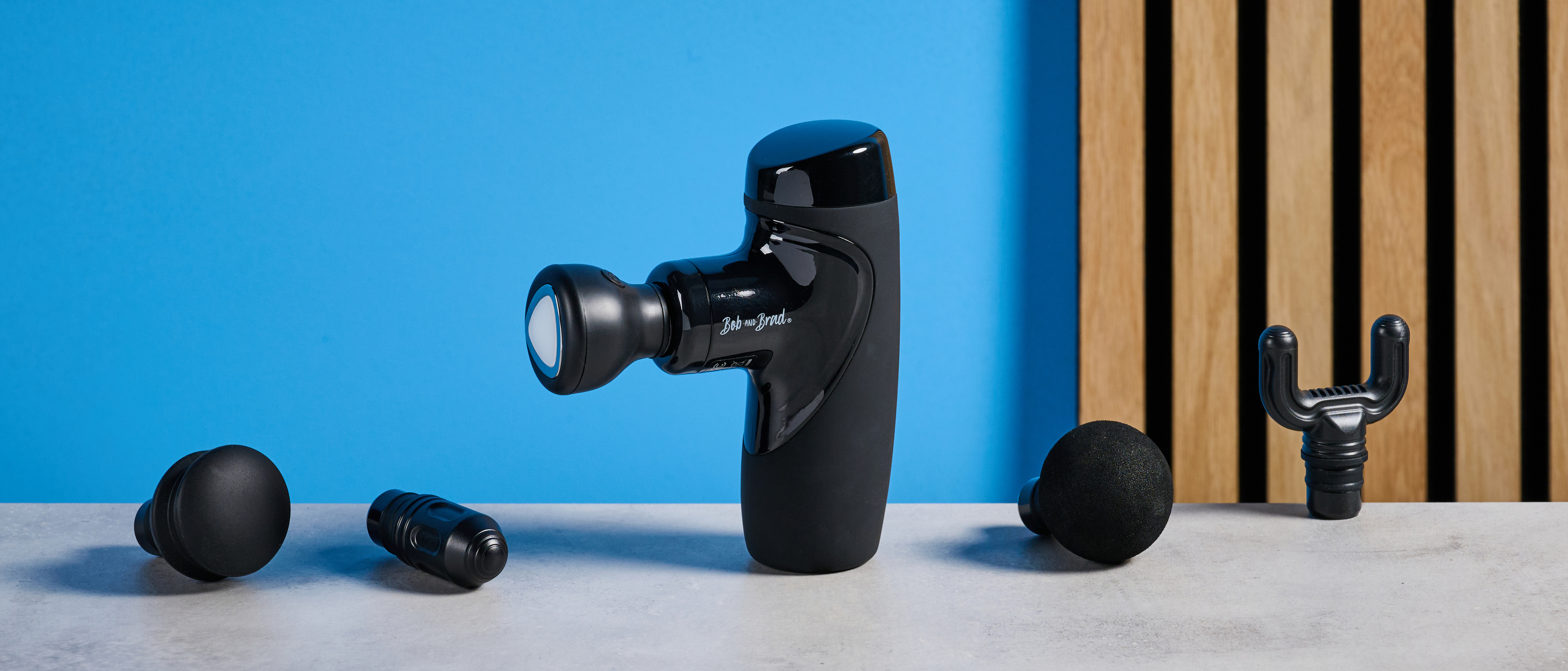 the bob and brad m7 plus mini massage gun in black with 5 attachments including a heat head photographed against a blue background