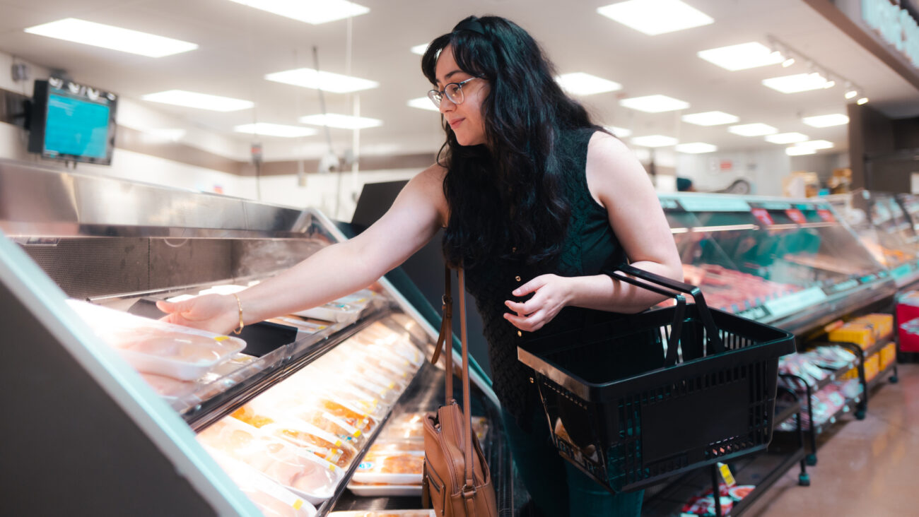Woman reaches for packet from open refrigerated shelving in a grocery store