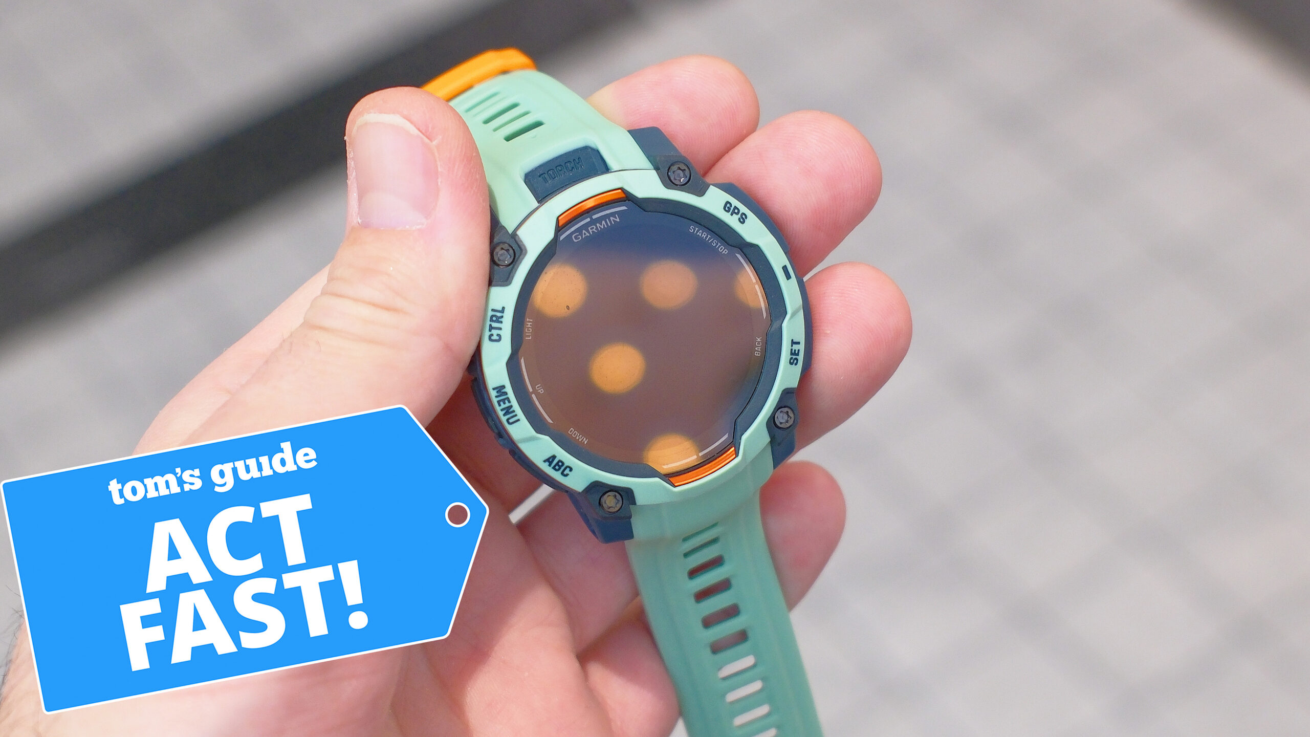 Garmin Instinct 3 in teal in a user's hand next to a deals badge