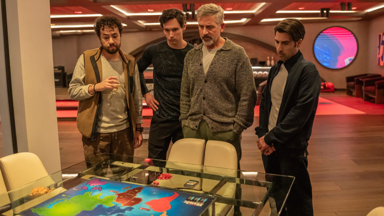 L-R: Ramy Youssef, Cory Michael Smith, Steve Carell and Jason Schwartzman standing looking at a RISK board in a scene from HBO Max's "Mountainhead"
