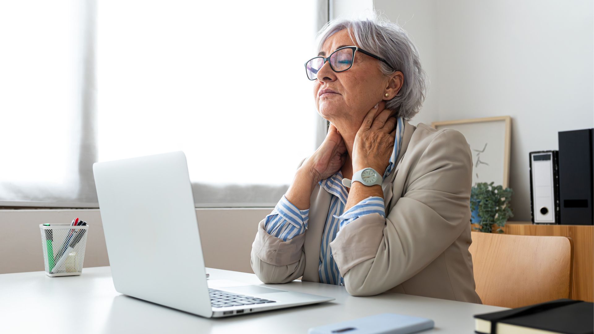 woman at desk holds neck in pain