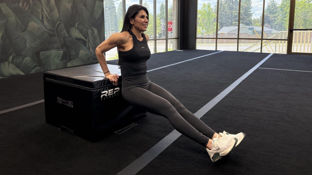 Woman exercising in empty gym space, performing a triceps dip with a plyo box