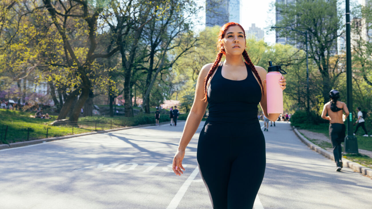Woman walking in Central Park holding large pink water bottle