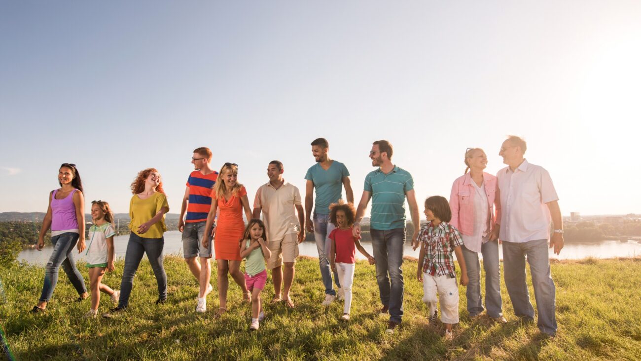 A group of people of mixed ages walk through a field. All look happy and are engaging with one another.