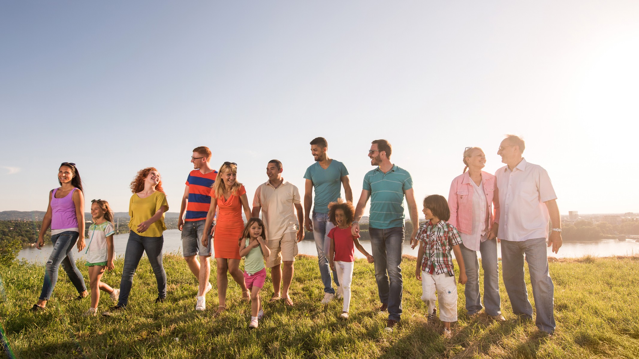 A group of people of mixed ages walk through a field. All look happy and are engaging with one another.