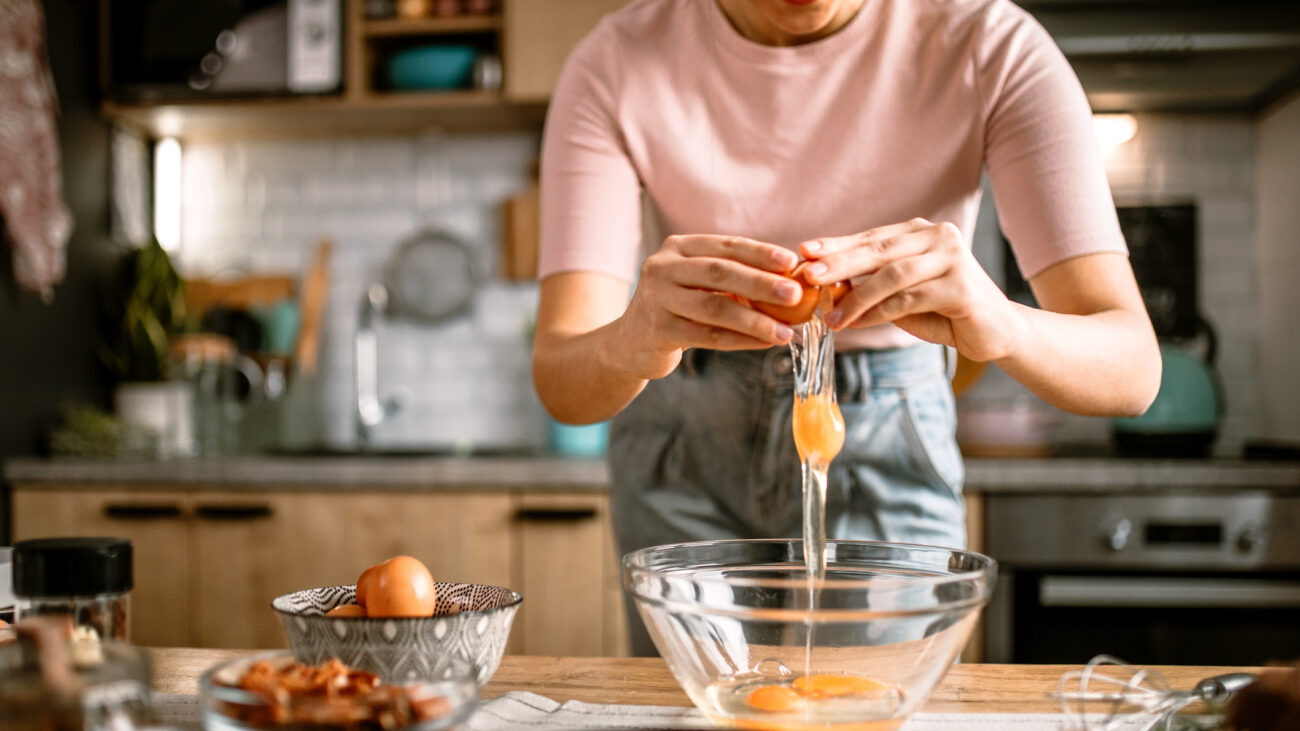 Torso of woman seen cracking eggs into a bowl in a kitchen