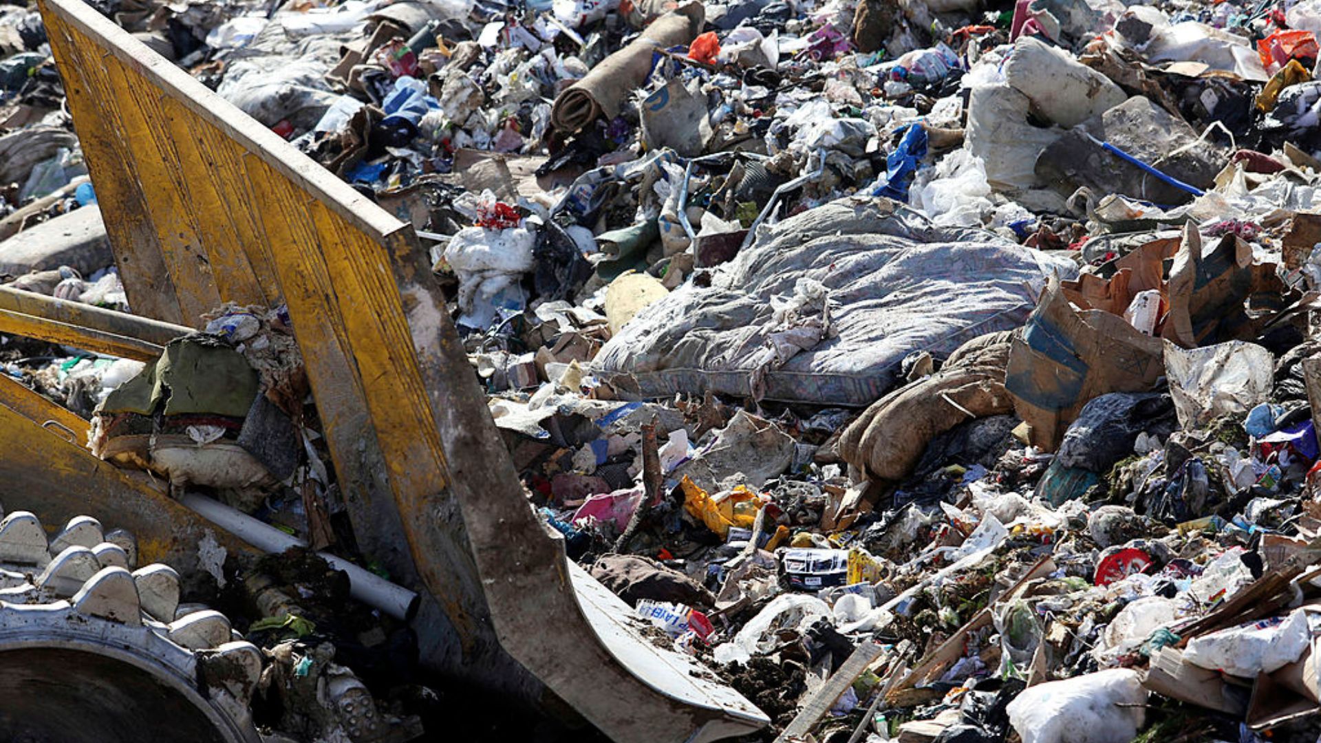A digger pushing a discarded mattress in a pile of rubbish in landfill
