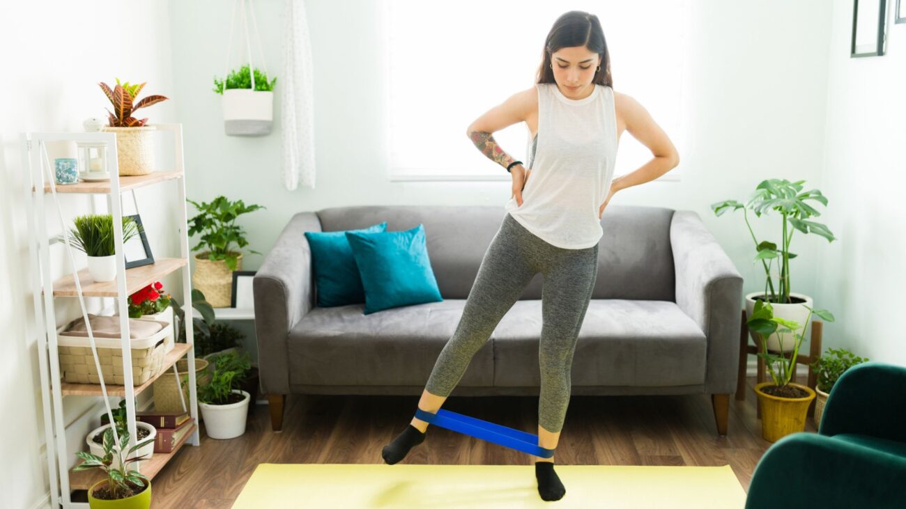 woman stands on yoga mat with resistance band around ankles