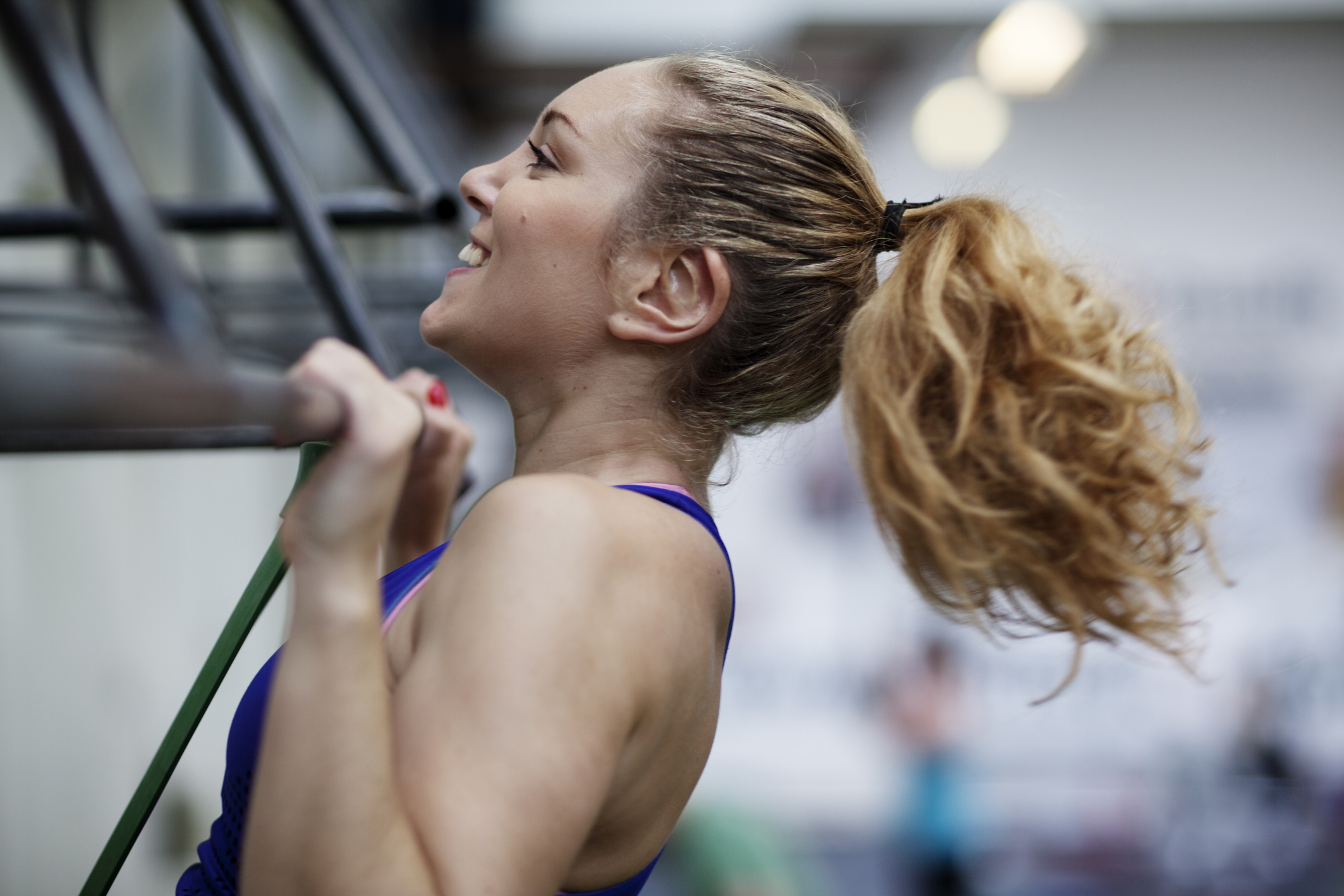 Smiling woman performing a pull-up in a gym, with her chin above the bar