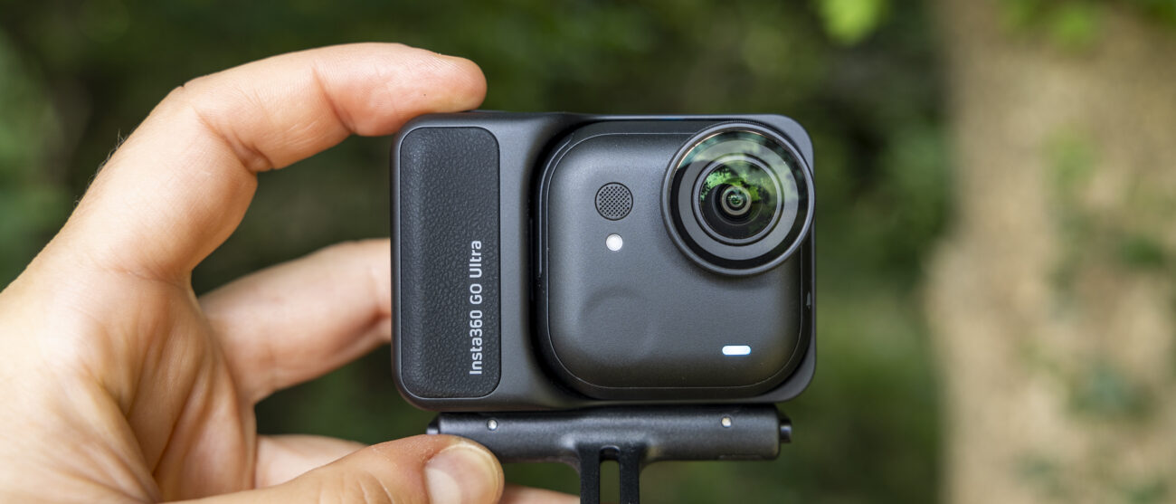 The Insta360 GO Ultra camera held by a female photographer against a green wooded backdrop