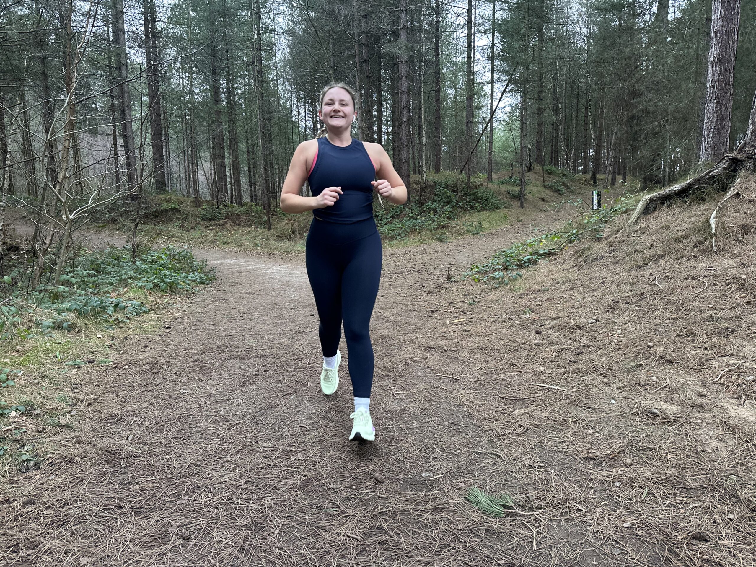 Fitness journalist Alice Porter runs through a forest in leggings and a vest.