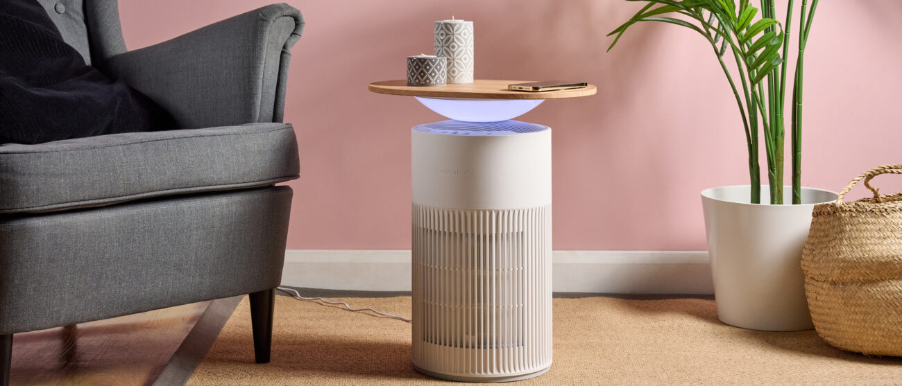 The SwitchBot Air Purifier Table is pictured in a pink living room. The ambient light below the tabletop is lit up blue.
