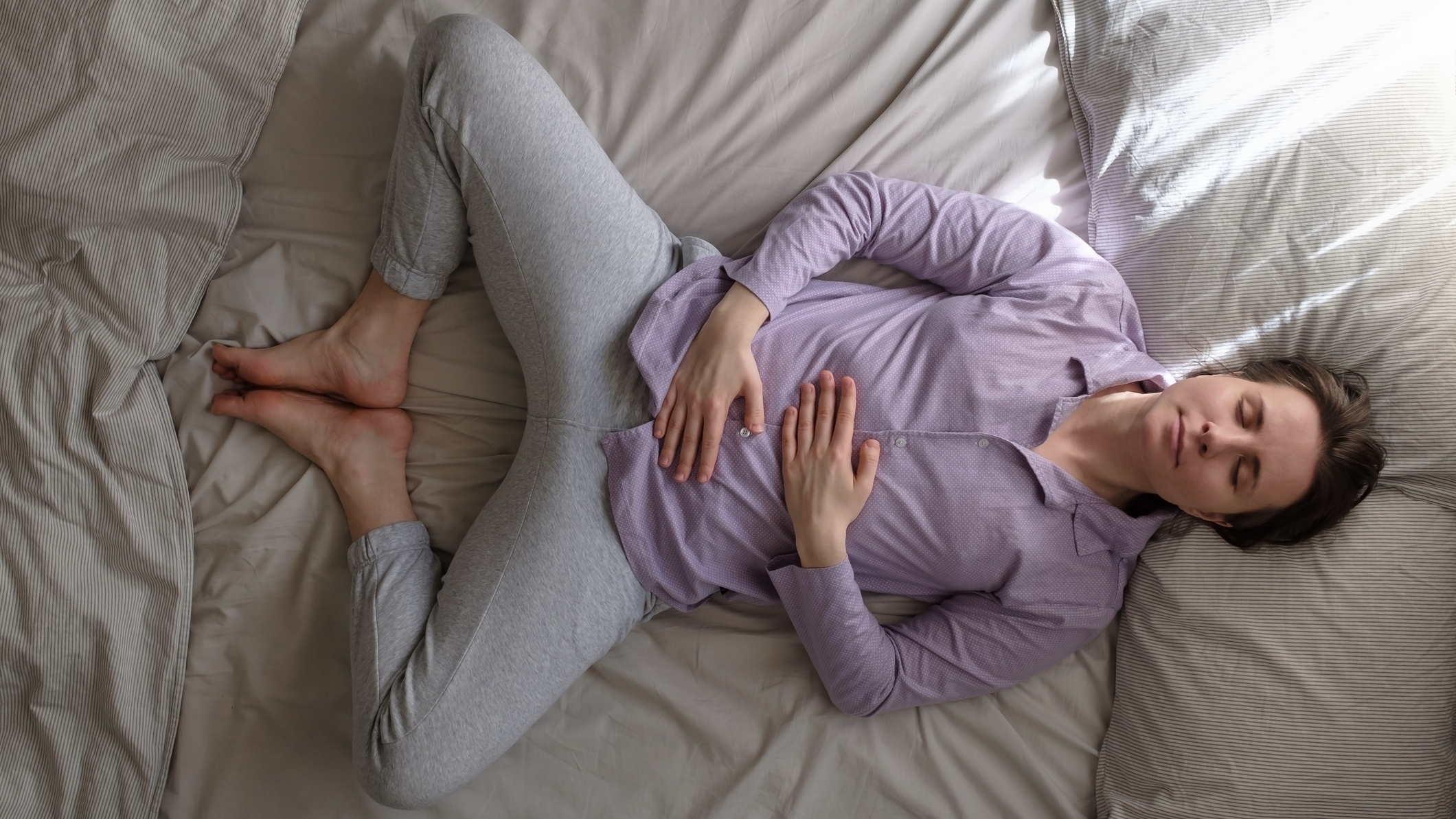 Woman lying on her back in bed in reclined bound angle yoga pose.
