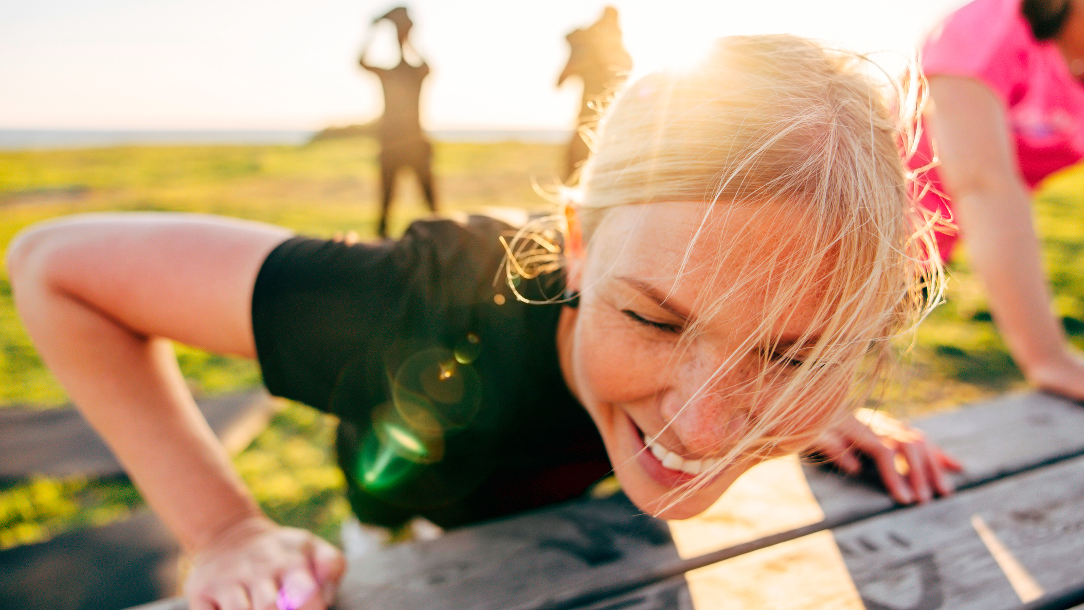 Woman outside smiling as she performs push-ups on a wooden bench